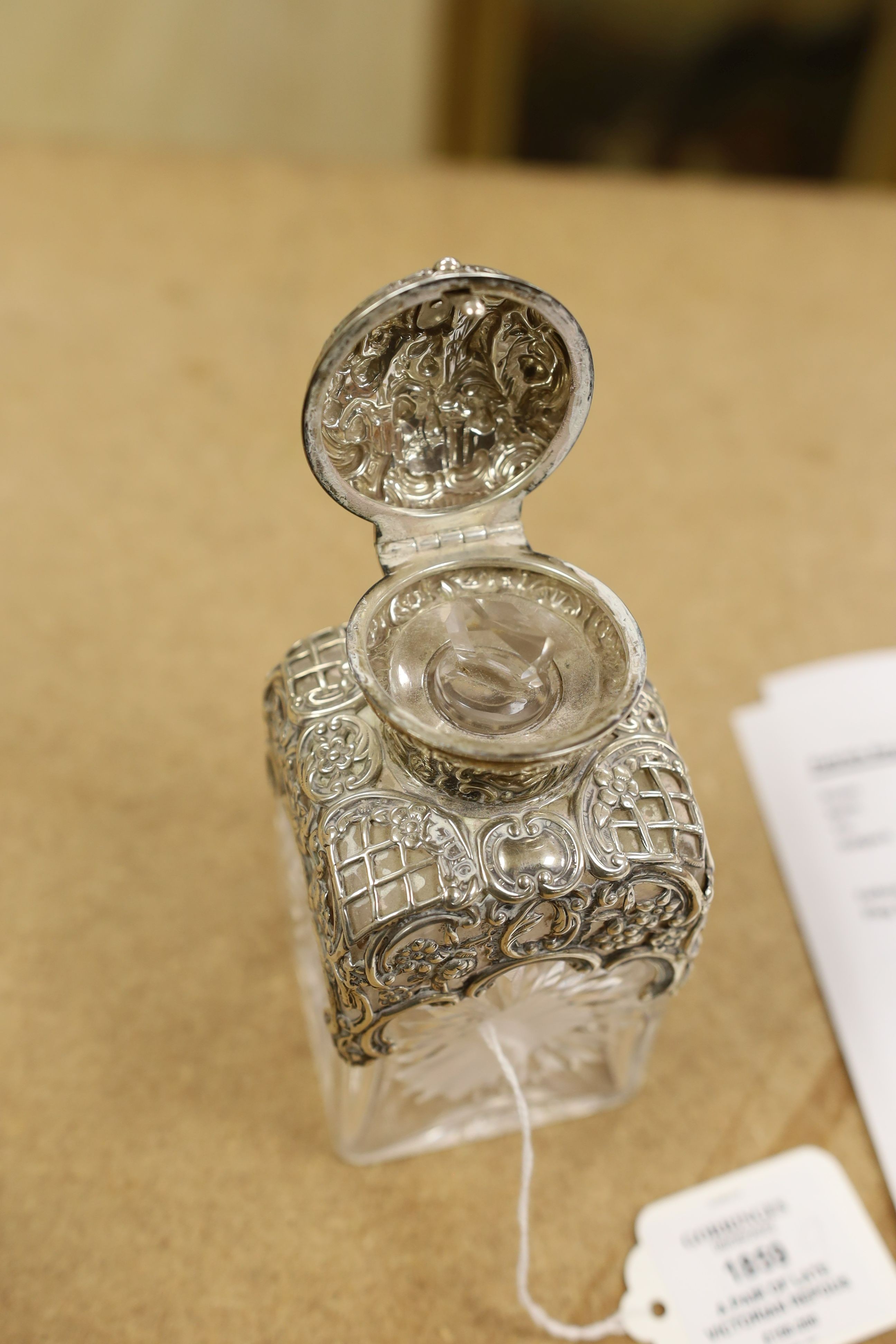 A pair of late Victorian repousse silver mounted cut glass scent bottles with stoppers, William Comyns, London, 1898, height 14.3cm.